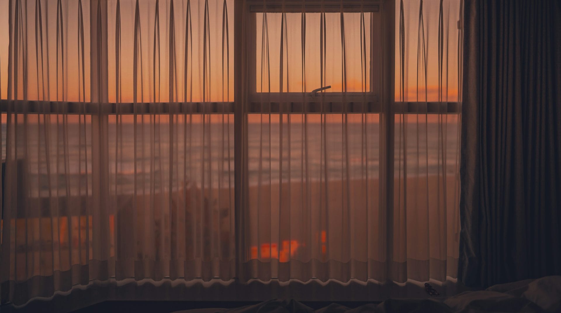 Beautiful image of the sunset looking at the ocean through windows whose blinds are closed.